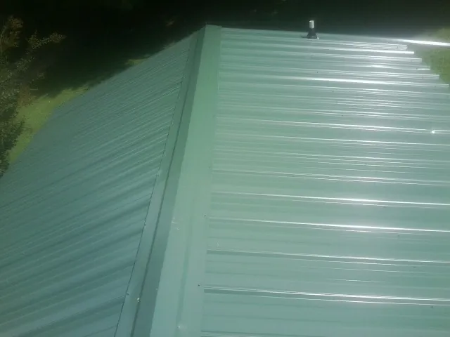 New green metal panels meeting at the ridge of a roof — Flat Roof Repair work by our crew in West Milton